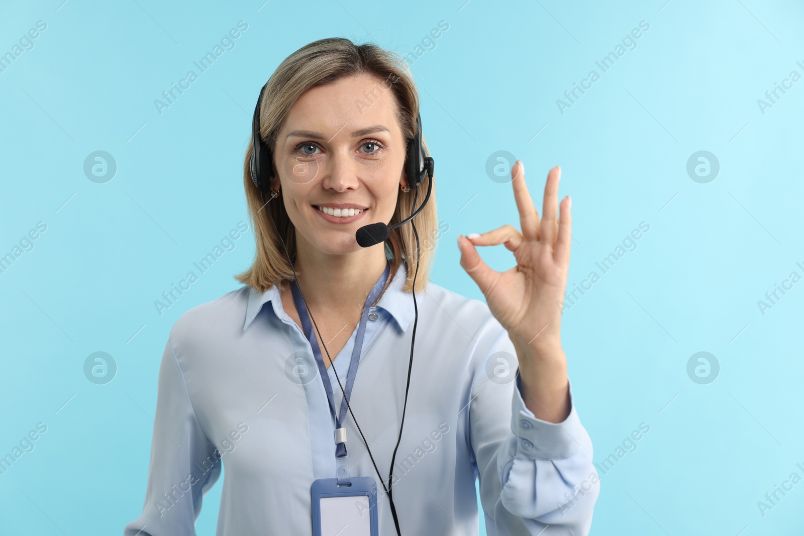 Photo of Technical support call center. Smiling operator showing ok gesture on light blue background