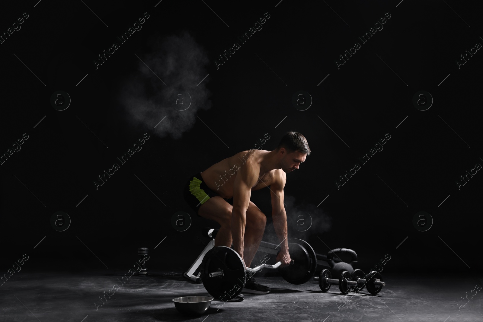 Photo of Man with talcum powder on hands training with barbell against black background