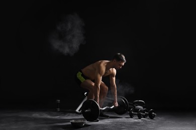 Photo of Man with talcum powder on hands training with barbell against black background