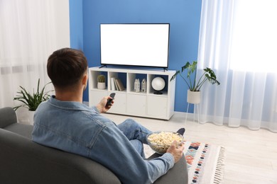 Photo of Man with popcorn watching tv on couch at home, back view