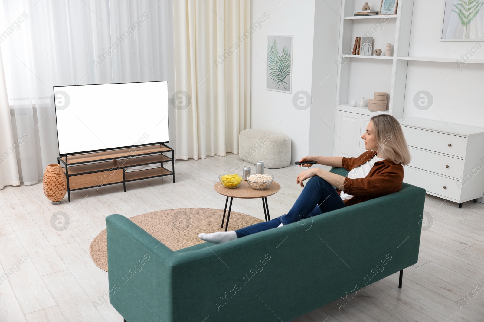 Photo of Woman with snacks and drinks watching tv on couch at home