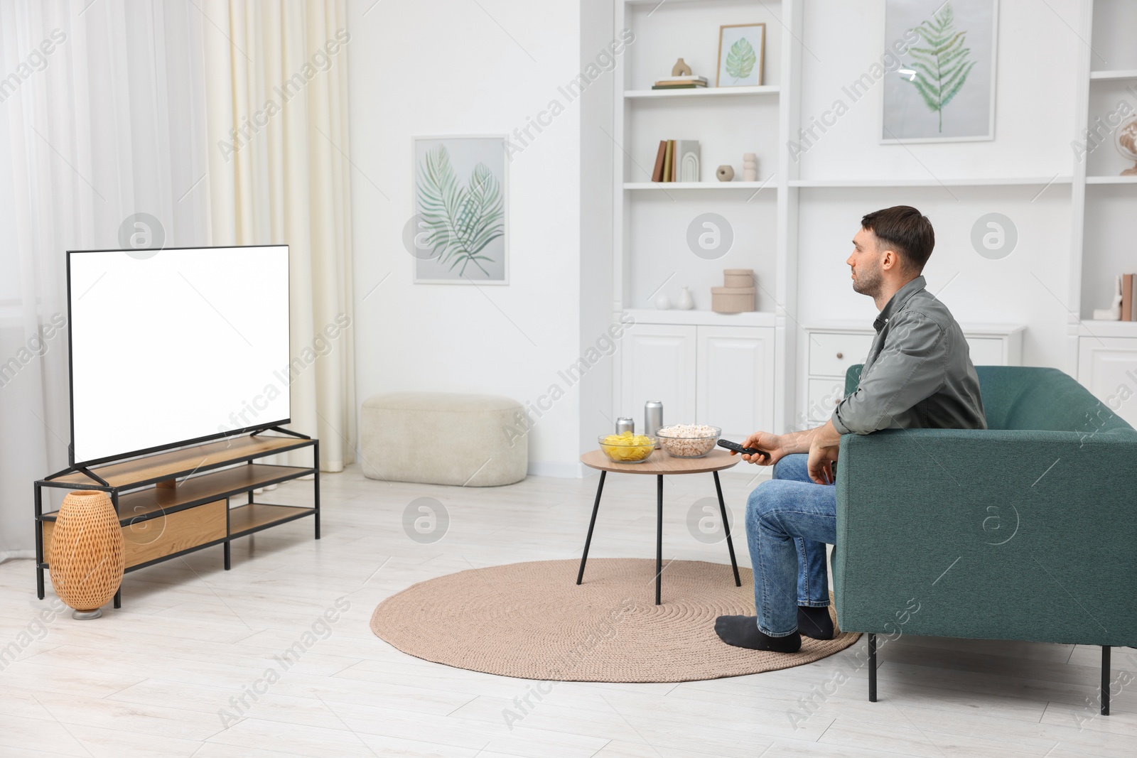 Photo of Man with snacks and drinks watching tv on couch at home