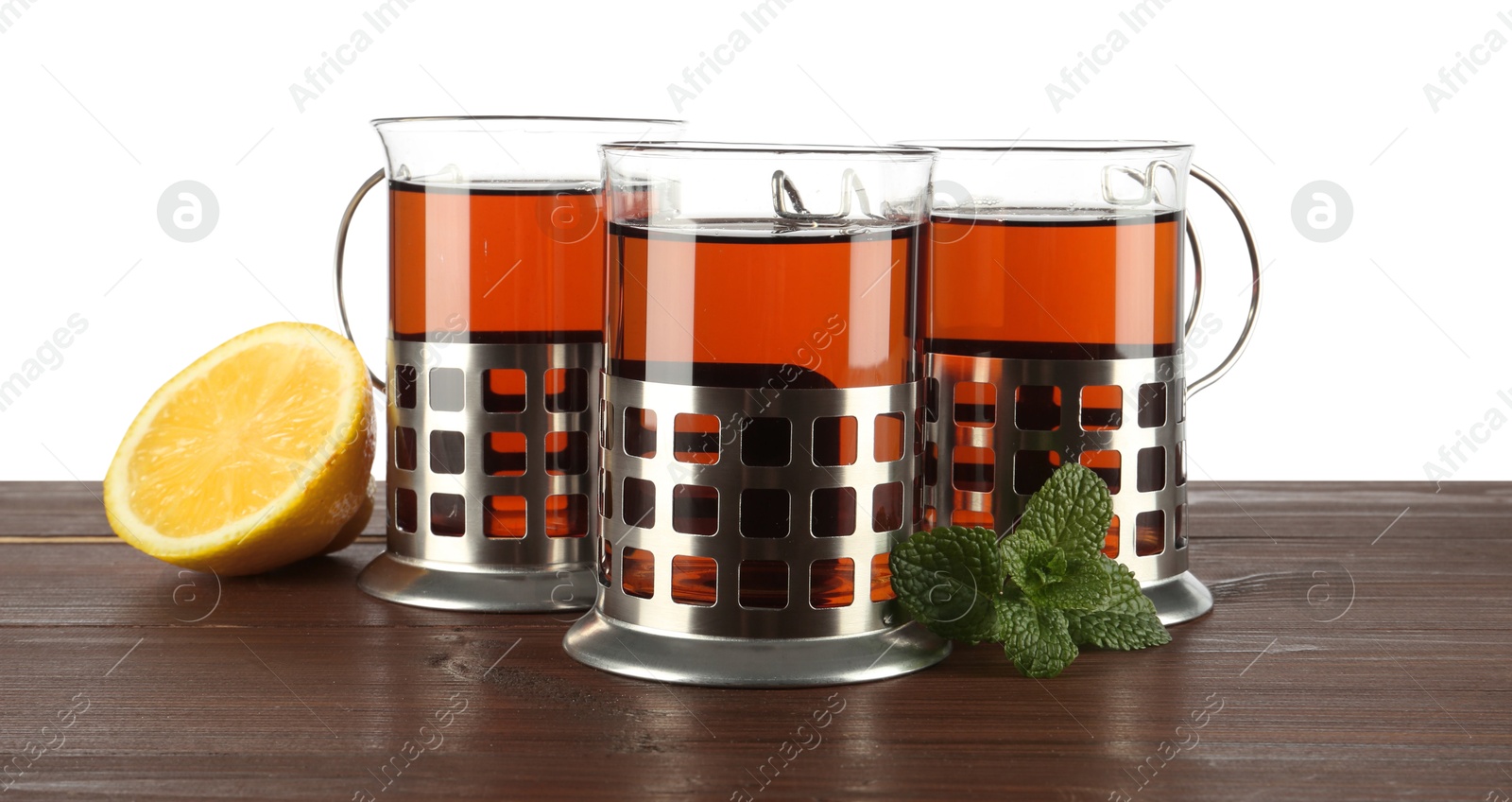 Photo of Glasses of aromatic tea in holders, lemon and mint on wooden table against white background