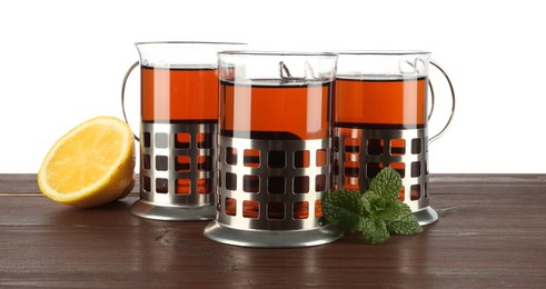 Glasses of aromatic tea in holders, lemon and mint on wooden table against white background