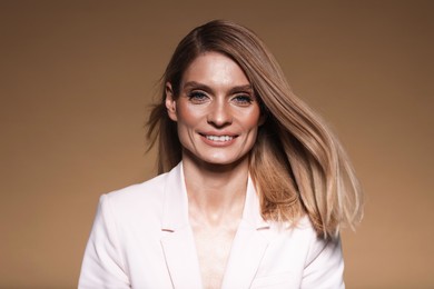 Portrait of beautiful happy woman with straight blonde hair on light brown background