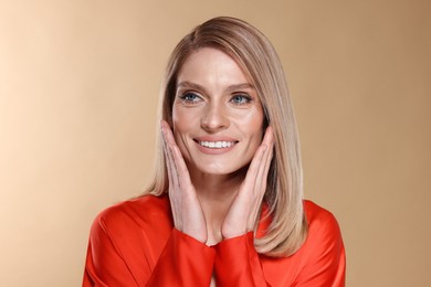 Portrait of beautiful happy woman with straight blonde hair on beige background