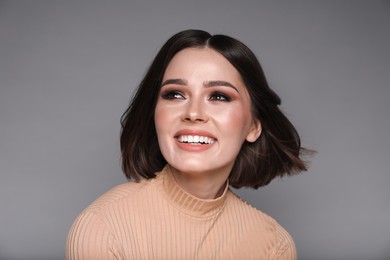 Portrait of beautiful young happy woman with gorgeous straight hair on grey background