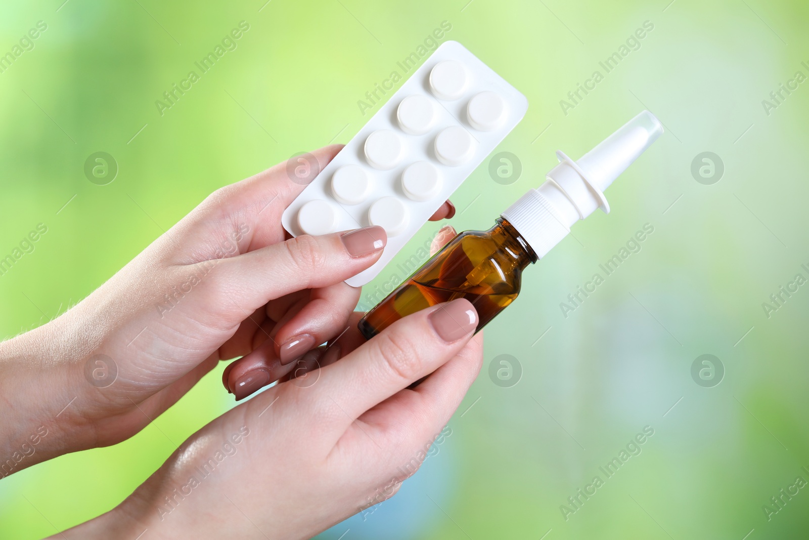 Photo of Allergy treatment. Woman with nasal spray and pills on blurred background, closeup