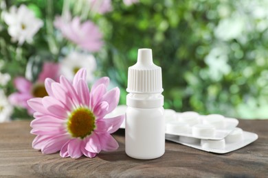 Photo of Allergy treatment. Bottle of medical drops, pills and flower on wooden table against blurred background, closeup