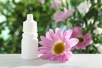 Photo of Allergy treatment. Bottle of medical drops and flower on white table against blurred background, closeup