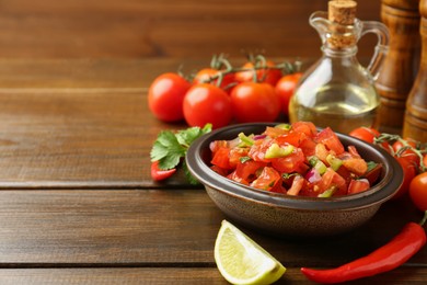 Photo of Delicious spicy salsa with ingredients on wooden table. Space for text