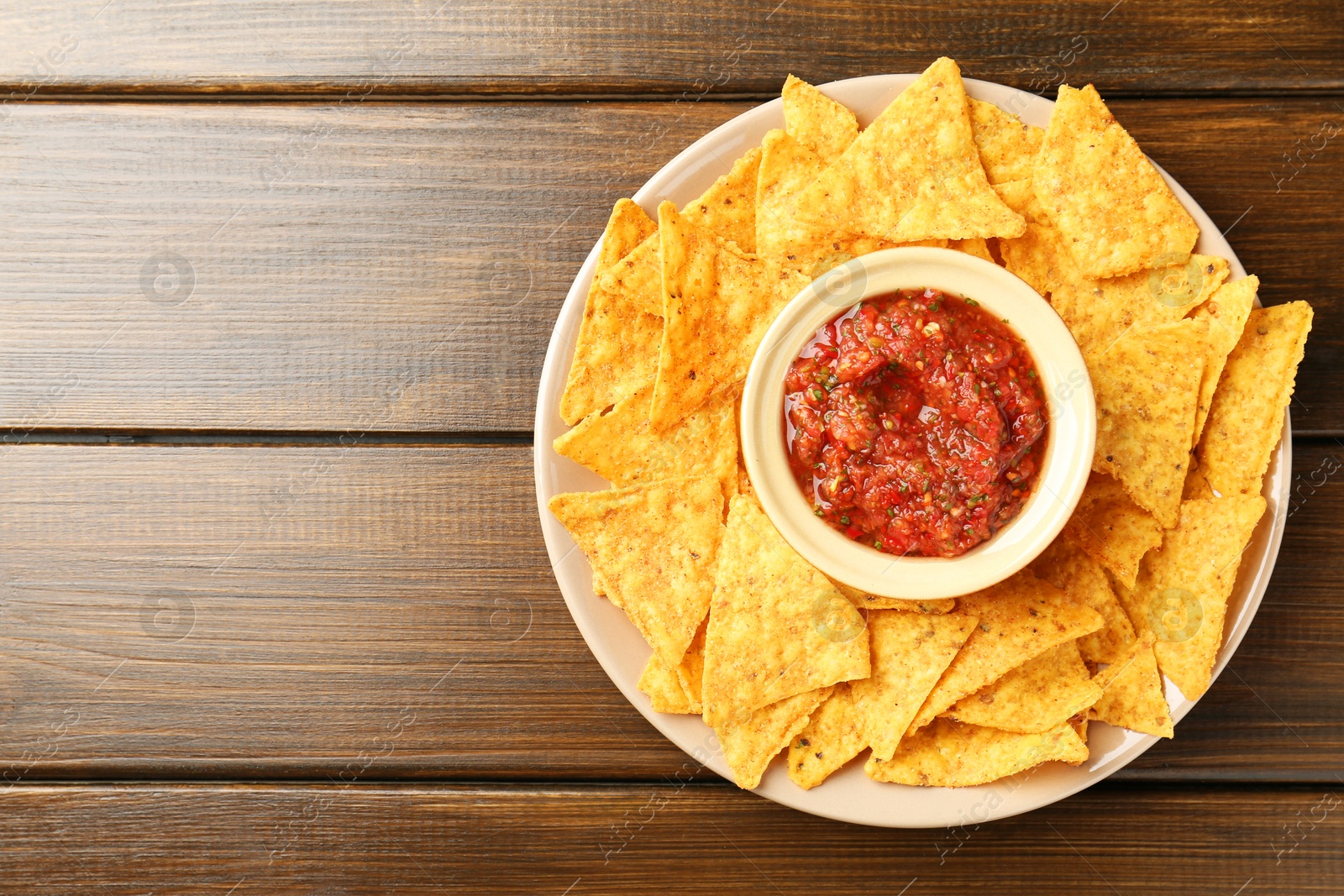 Photo of Delicious salsa with nachos on wooden table, top view. Space for text