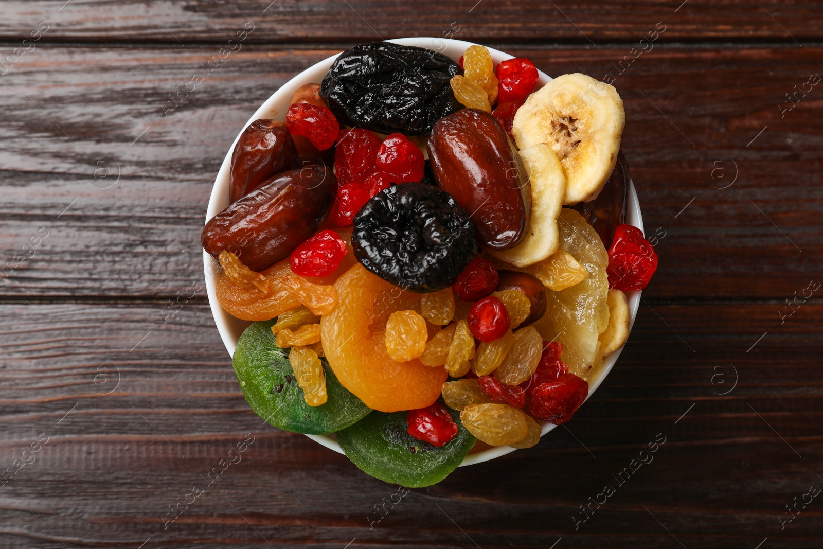 Photo of Mix of different dried fruits in bowl on wooden table, top view