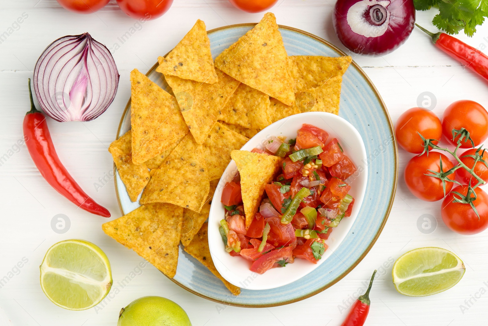 Photo of Delicious salsa (Pico de gallo) served with nachos among products on white wooden table, flat lay