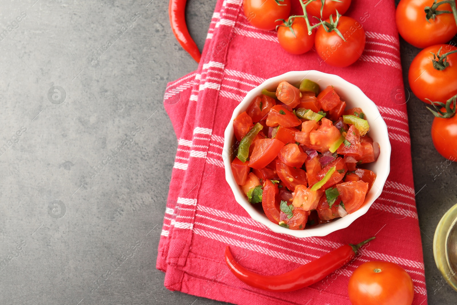 Photo of Delicious salsa (Pico de gallo) in bowl and ingredients on grey textured table, flat lay. Space for text