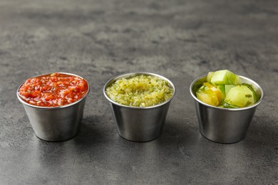 Photo of Different types of salsa in bowls on grey textured table, closeup