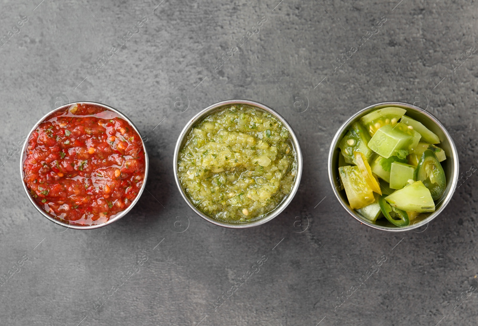 Photo of Different types of salsa in bowls on grey textured table, flat lay