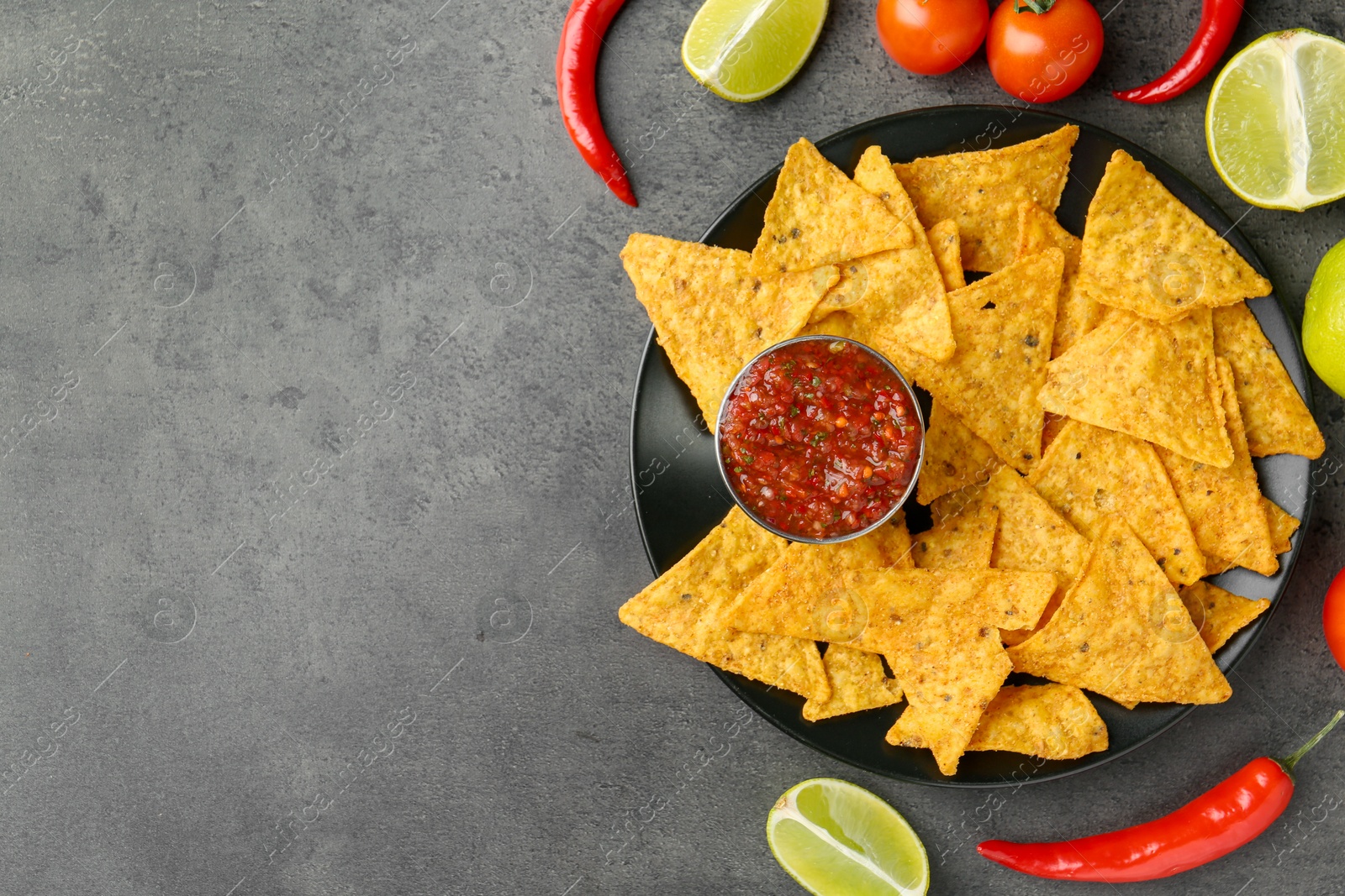 Photo of Delicious salsa sauce served with nachos and products on grey textured table, flat lay. Space for text