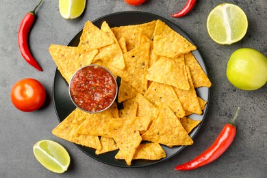 Photo of Delicious salsa sauce served with nachos and products on grey textured table, flat lay