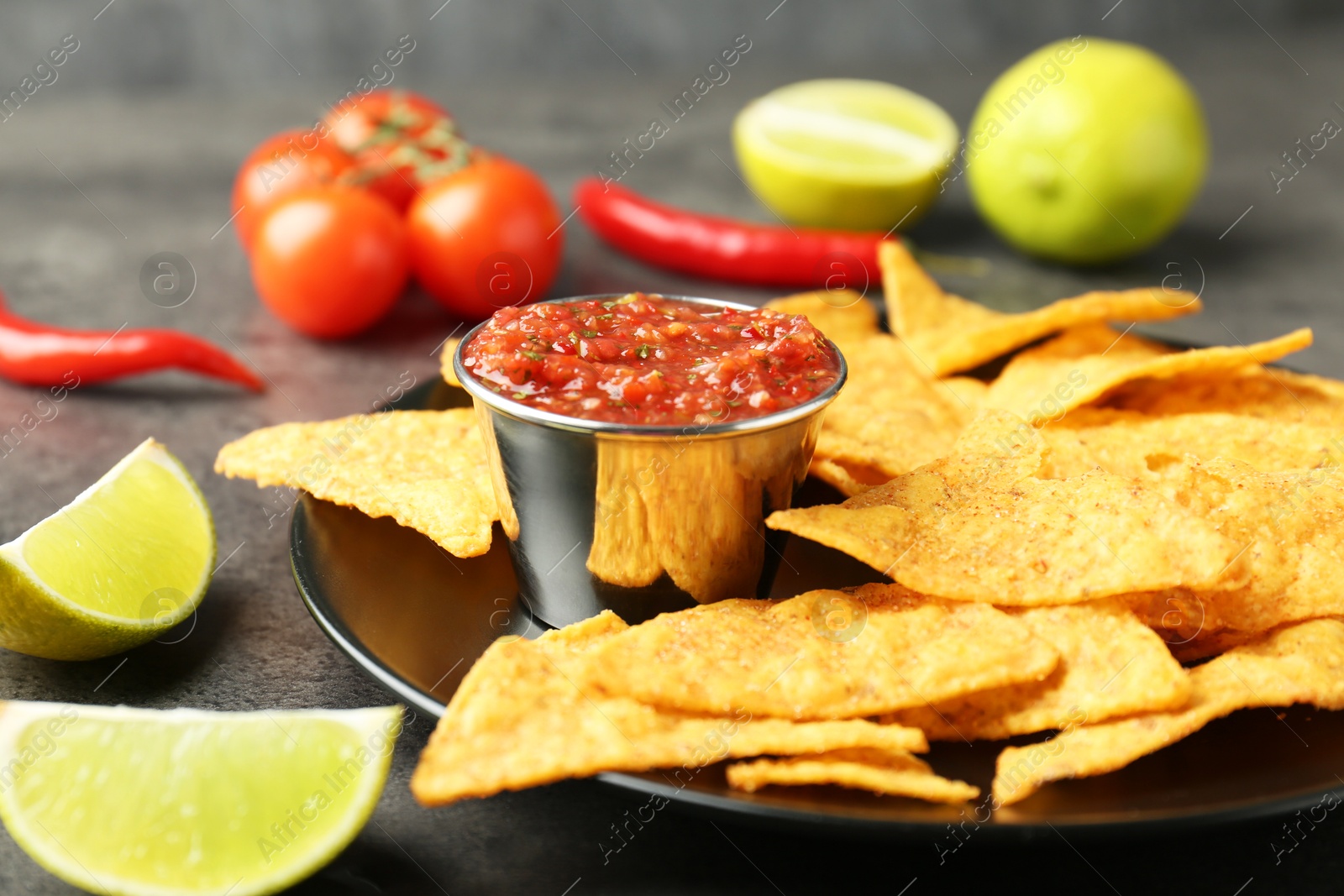 Photo of Delicious salsa sauce served with nachos and products on grey textured table, closeup