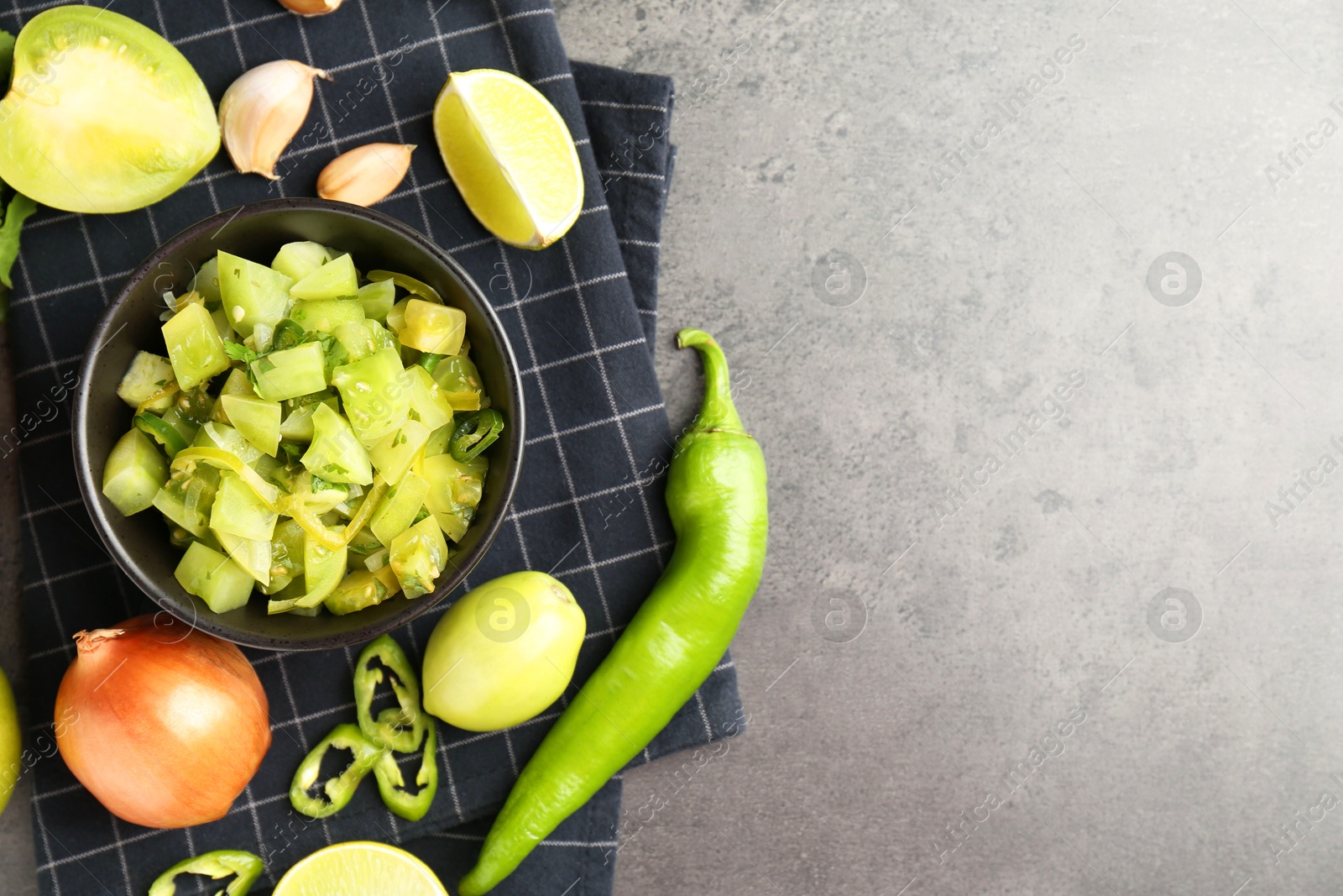 Photo of Delicious salsa (Pico de gallo) in bowl and products on grey textured table, flat lay. Space for text