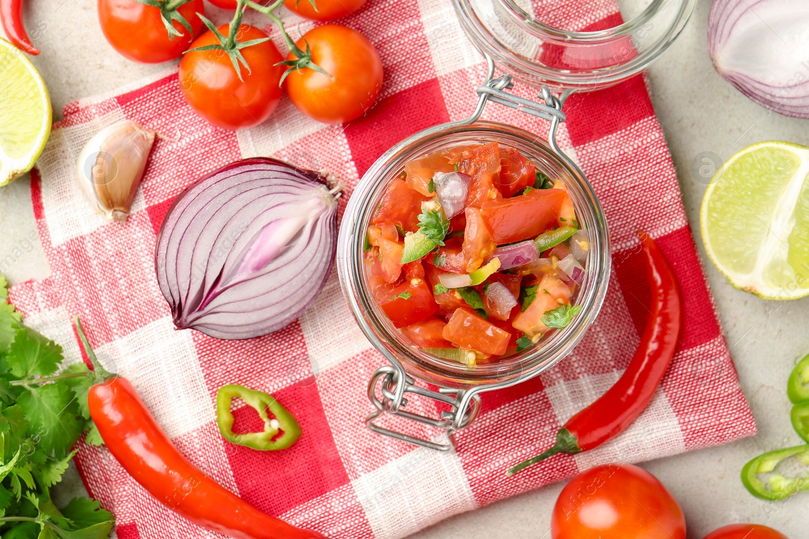 Photo of Delicious salsa (Pico de gallo) in jar and ingredients on light textured table, flat lay