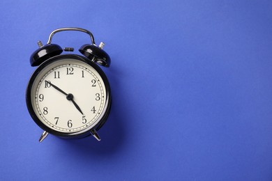 Photo of One black alarm clock on blue background, top view. Space for text