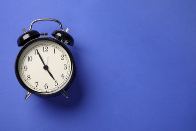 Photo of One black alarm clock on blue background, top view. Space for text