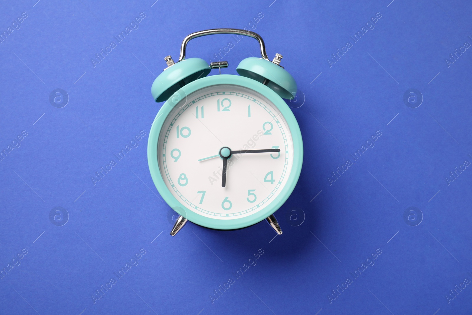 One turquoise alarm clock on blue background, top view Photo of One turquoise alarm clock on blue background, top view