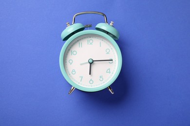 Photo of One turquoise alarm clock on blue background, top view