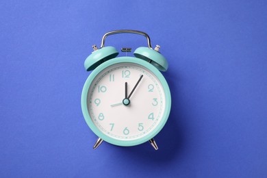 Photo of One turquoise alarm clock on blue background, top view