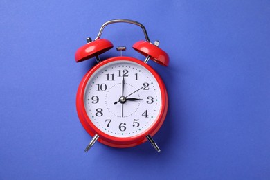 Photo of One red alarm clock on blue background, top view