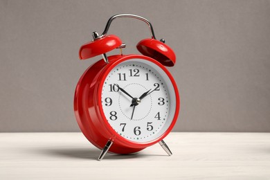 Photo of One red alarm clock on white wooden table against grey background