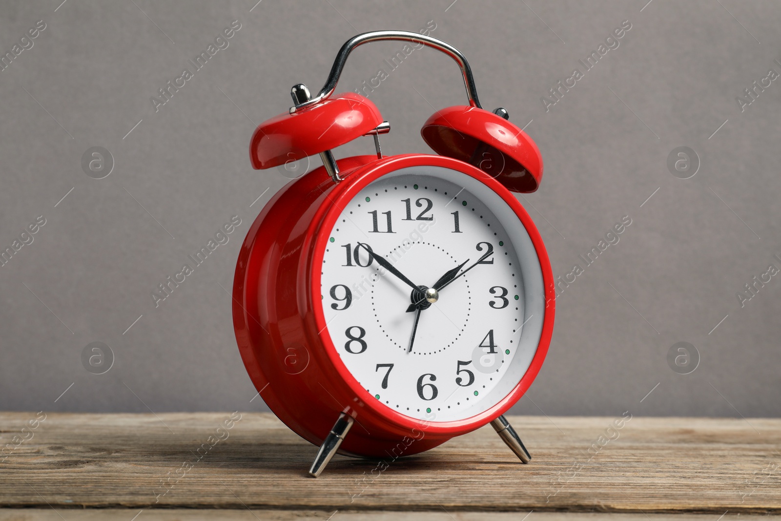 Photo of One red alarm clock on wooden table against grey background