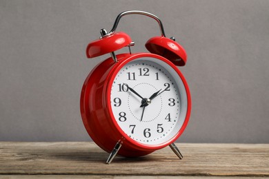 Photo of One red alarm clock on wooden table against grey background