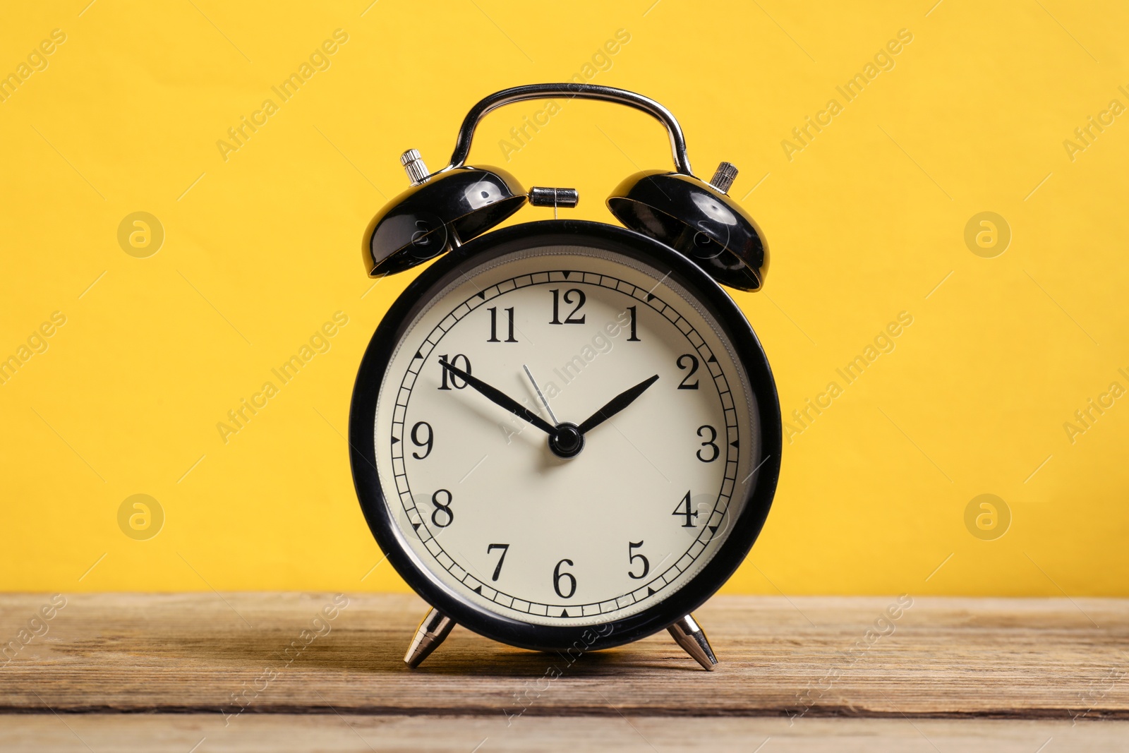 One black alarm clock on wooden table against yellow background Photo of One black alarm clock on wooden table against yellow background