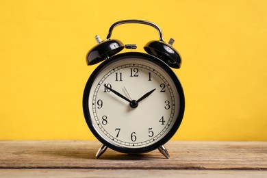 Photo of One black alarm clock on wooden table against yellow background