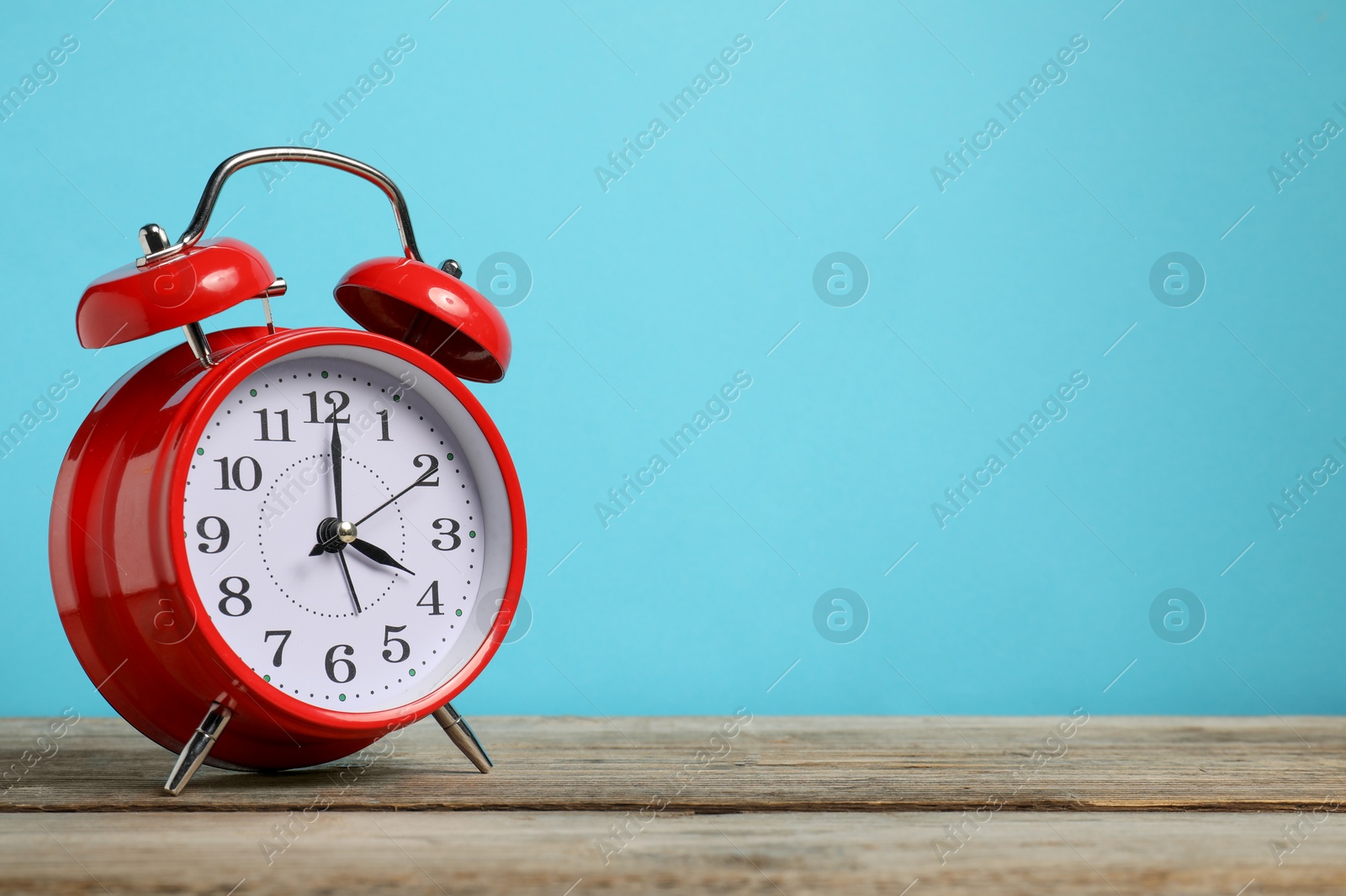 One red alarm clock on wooden table against light blue background, space for text Photo of One red alarm clock on wooden table against light blue background, space for text