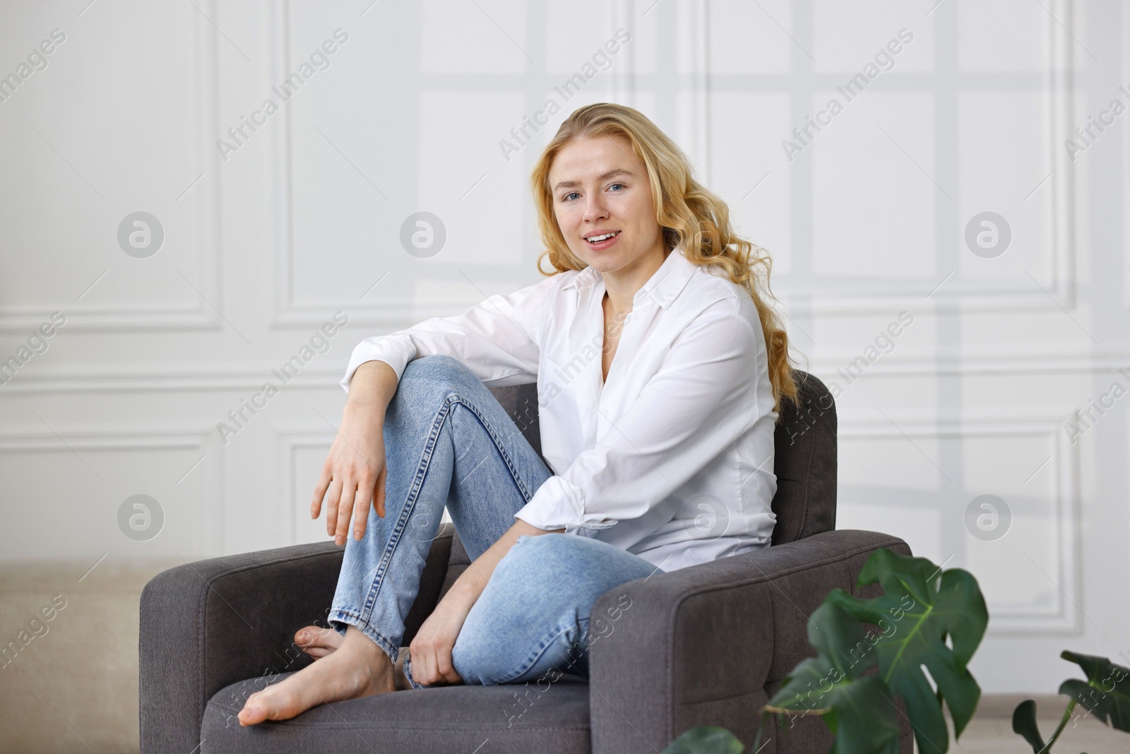 Photo of Smiling woman in stylish jeans sitting on armchair at home