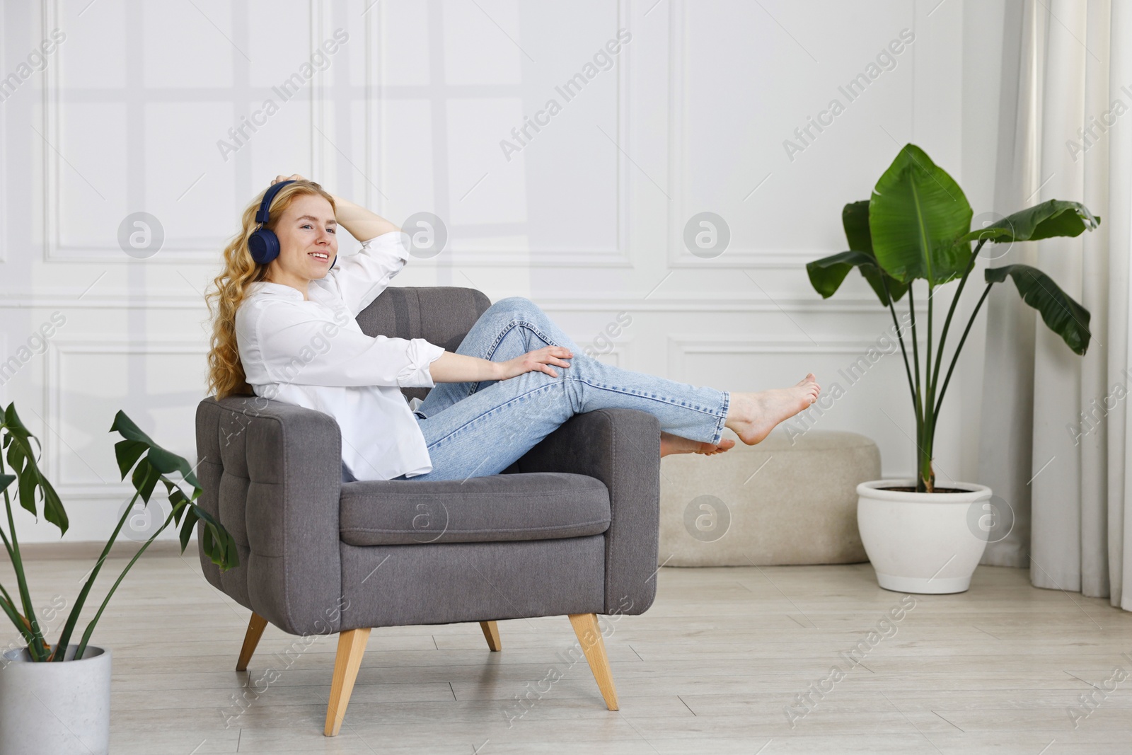 Photo of Smiling woman in stylish jeans listening to music on armchair at home