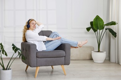 Photo of Smiling woman in stylish jeans listening to music on armchair at home