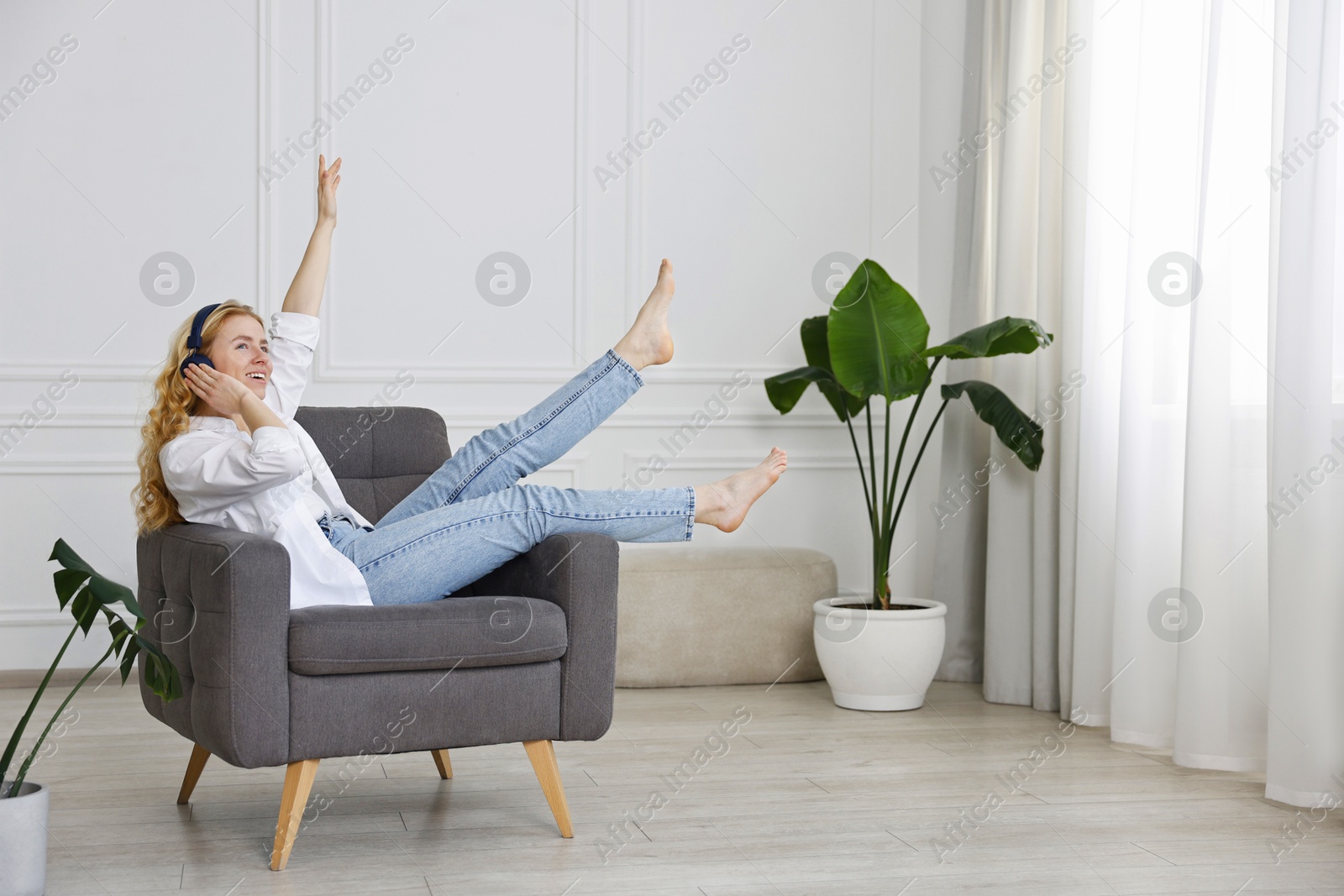 Photo of Smiling woman in stylish jeans listening to music on armchair at home