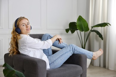 Photo of Smiling woman in stylish jeans listening to music on armchair at home