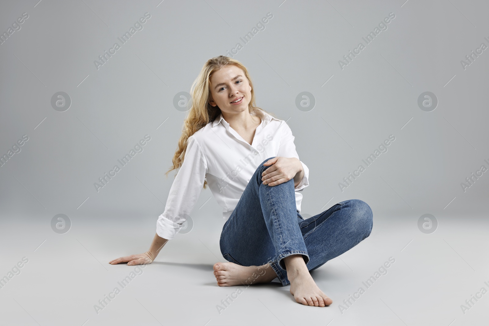 Photo of Smiling woman in stylish jeans on grey background