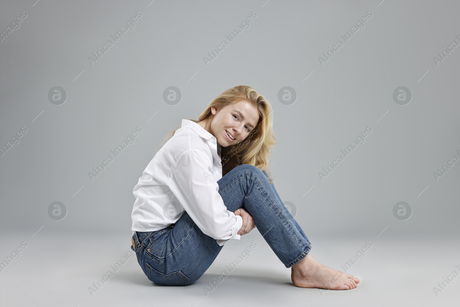 Photo of Smiling woman in stylish jeans on grey background