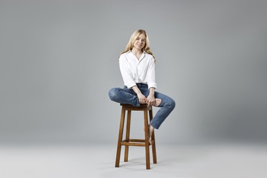 Photo of Smiling woman in stylish jeans sitting on stool against grey background