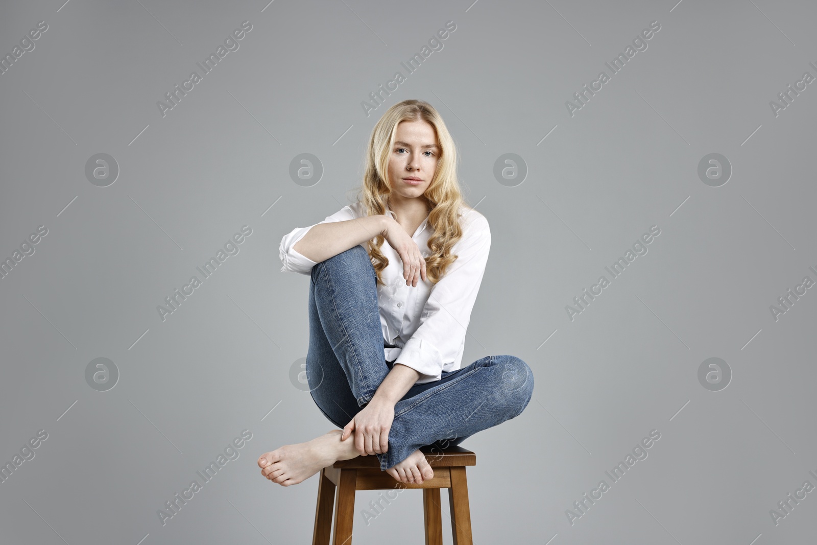 Photo of Beautiful young woman in stylish jeans sitting on stool against grey background