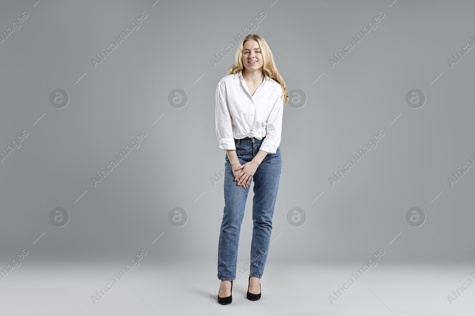 Photo of Smiling woman in stylish jeans on grey background