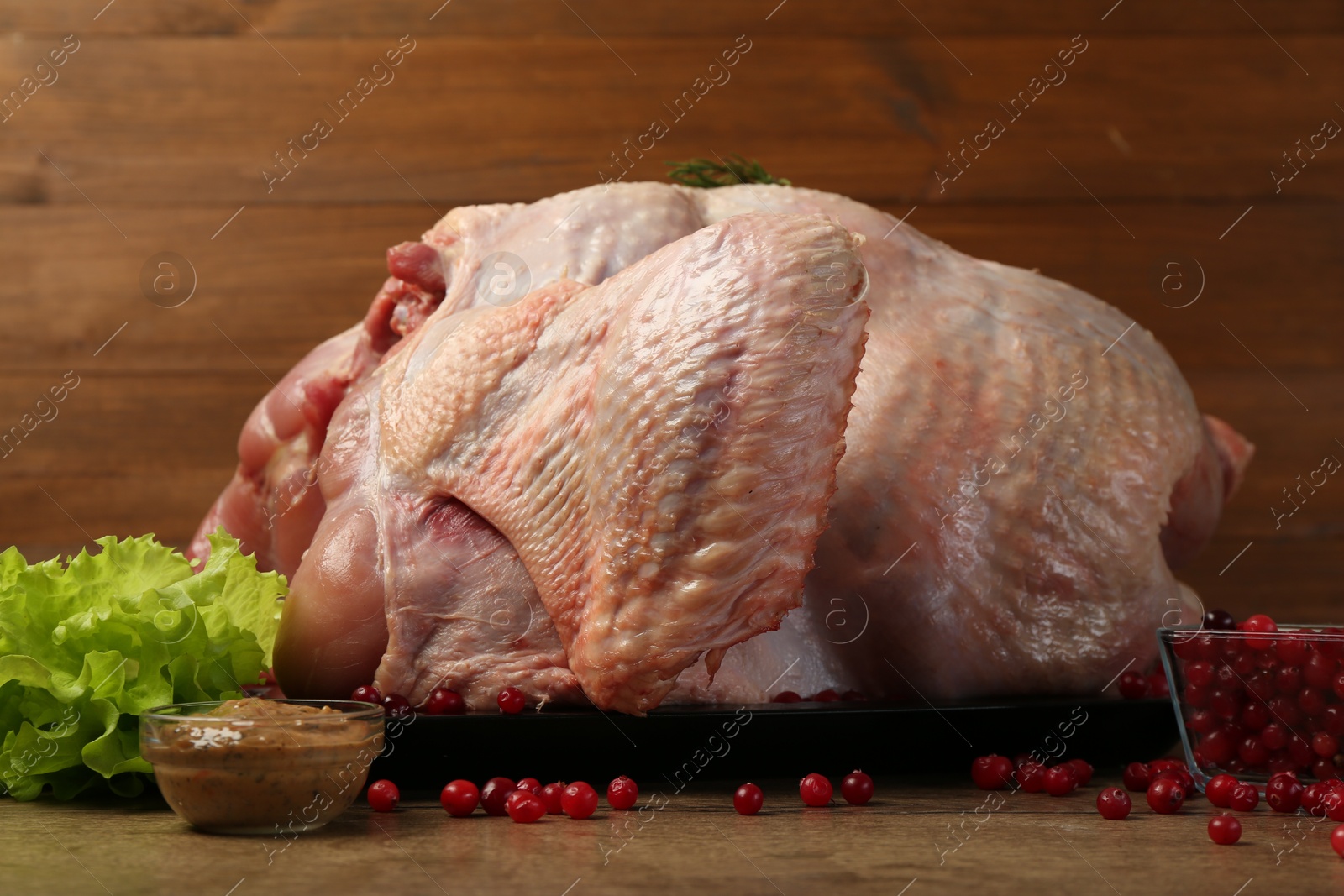 Photo of Whole raw turkey, marinade, cranberries and lettuce on wooden table