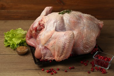 Photo of Whole raw turkey, marinade, cranberries and lettuce on wooden table